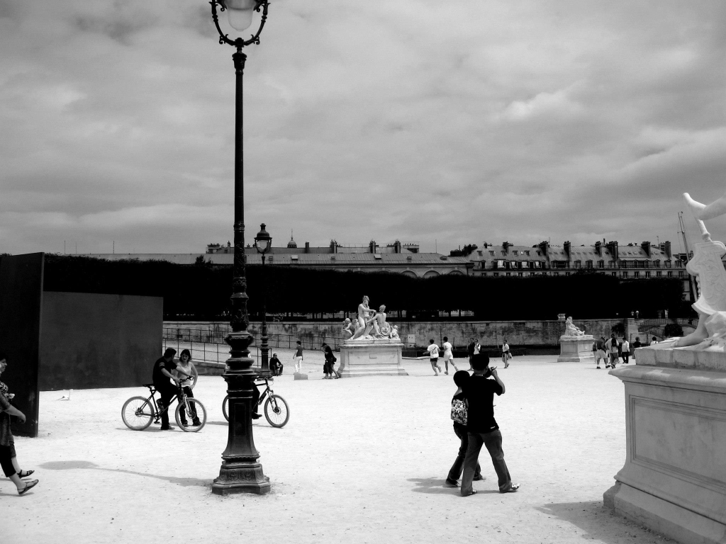 Schwarzweißfotografie eines Pariser Platzes mit Laterne, Skulpturen und Passanten